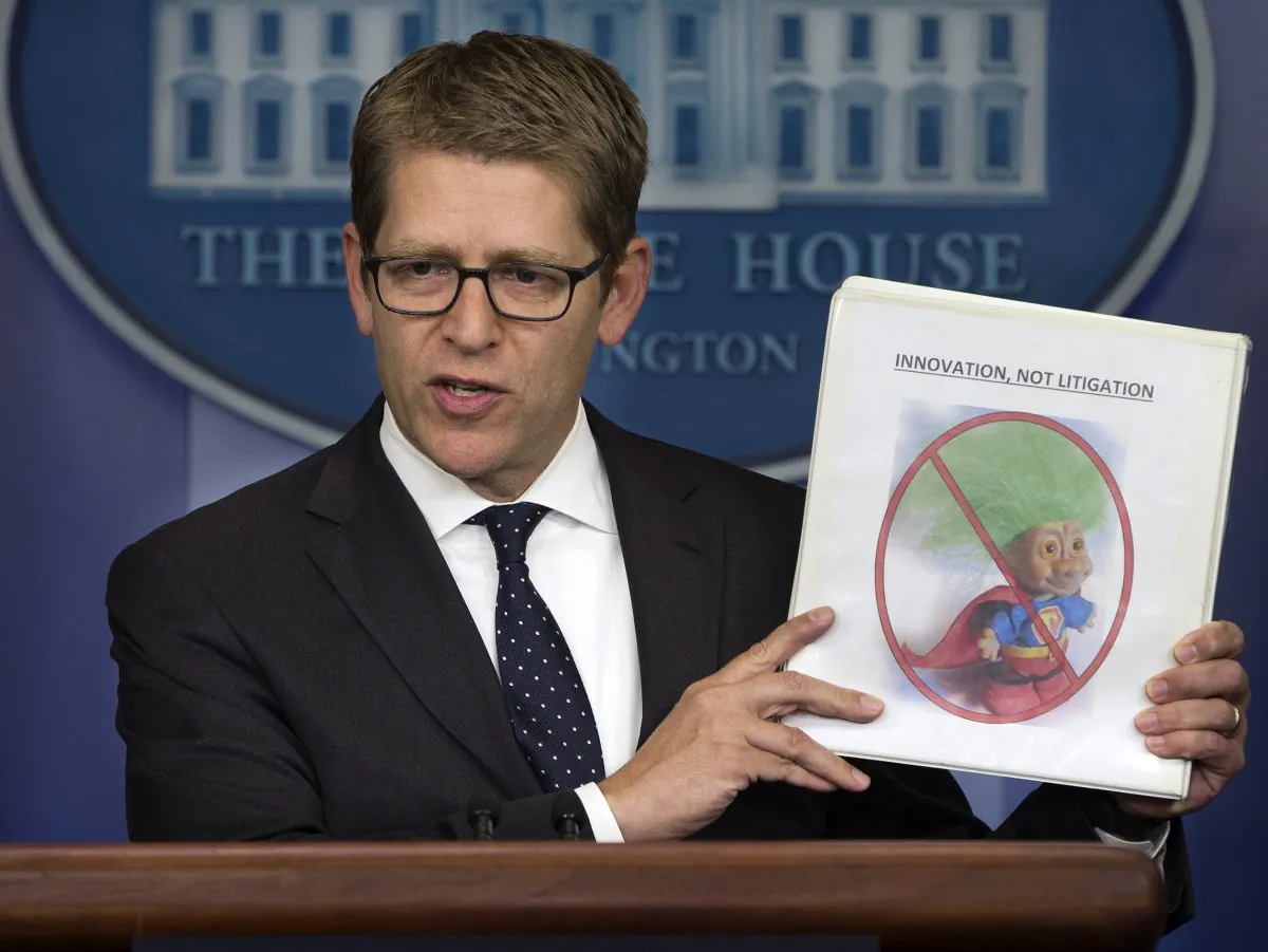 White House press secretary Jay Carney holds up a folder with an image of a troll and the words "innovation, not litigation" during the daily press briefing at the White House in Washington, D.C., on June 4, 2013. (AP Photo/Evan Vucci)