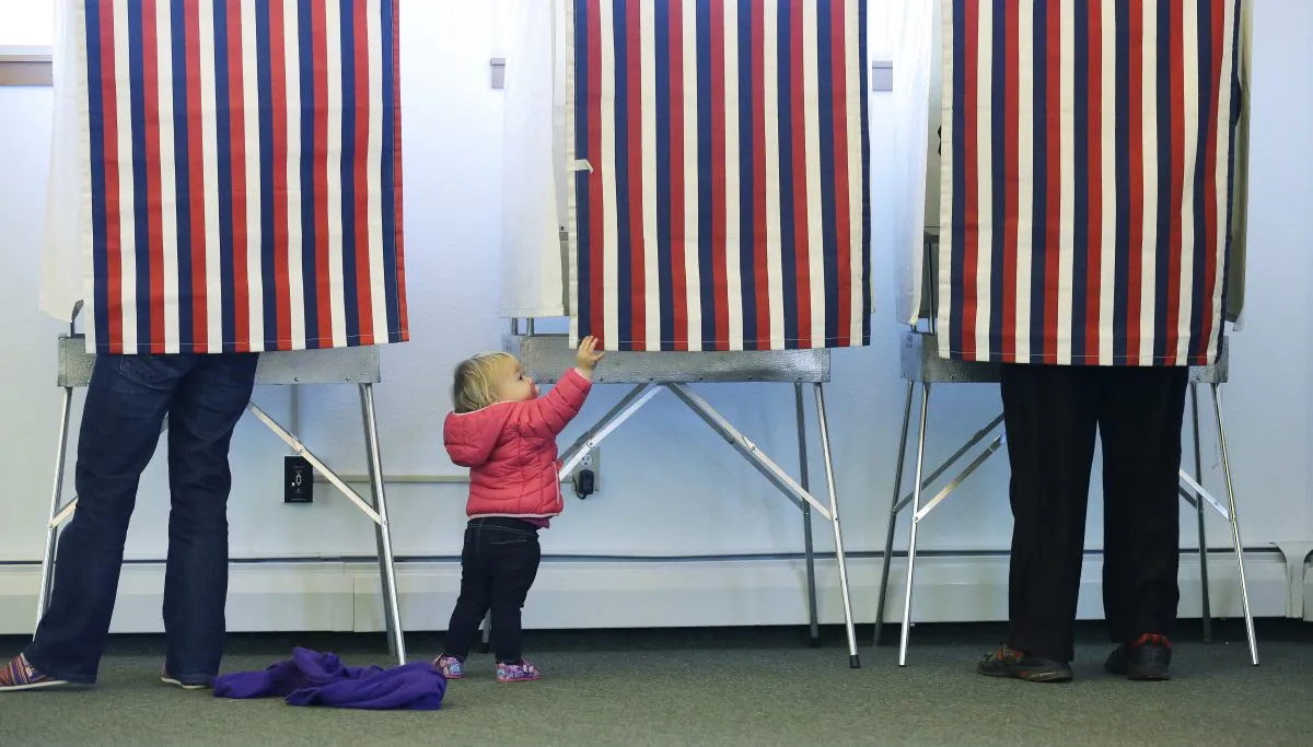 Zoe Buck, 14 months old, checks out an empty voting booth as her mother, Julie Buck (L), votes at the Alaska Zoo polling place in Anchorage, Alaska, on Nov. 4, 2014. (Ted S. Warren/AP Photo)