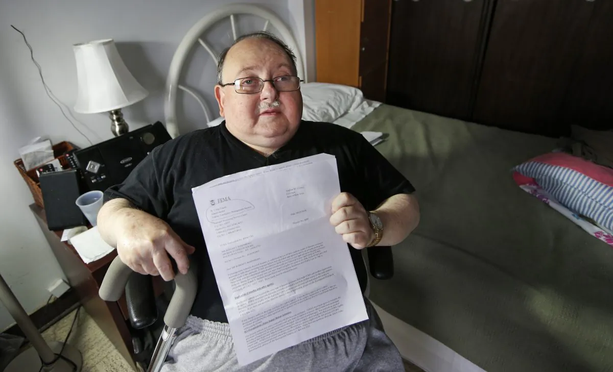 Belle Harbor Manor resident Robert Rosenberg, 61, who suffers from a spinal disability and has other chronic health problems, sits in his room in an assisted living facility in New York on Nov. 6, 2014. Rosenberg holds a letter from the Federal Emergency Management Agency asking him to pay back all the federal disaster aid he received after the storm. He is among a dozen residents of Belle Harbor Manor who have been asked to return aid money. (AP Photo/Kathy Willens)