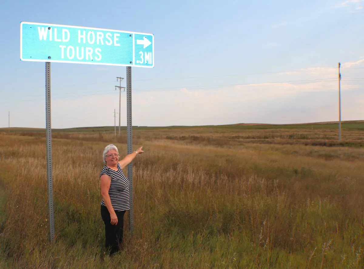 Karen Sussman ISPMB President pointing to road sign that indicates the ranch. Visitors are welcome. The conservancy is 12 miles from Eagle Butte, South Dakota. Few there are that venture 2 1/2 hours from Rapid City to see the amazing horses under Karen's watch. (Myriam Moran copyright 2014)