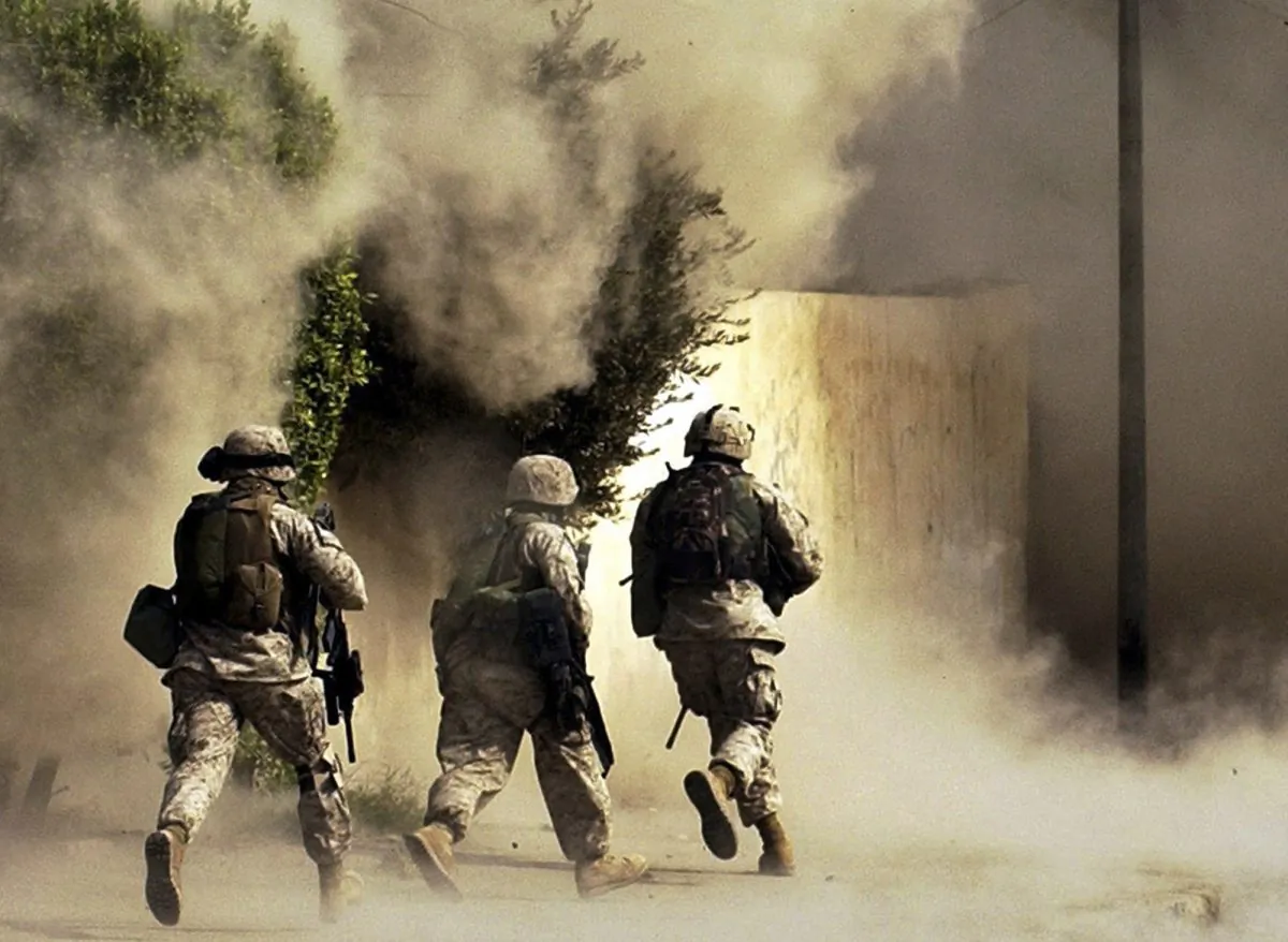 US Marines from the 2nd Battalion, 5th Marine Regiment, run to a building after detonating explosives to open a gate during a mission in Ramadi in Anbar province, Iraq, on Oct. 26, 2004.  (AP Photo/Jim MacMillan)