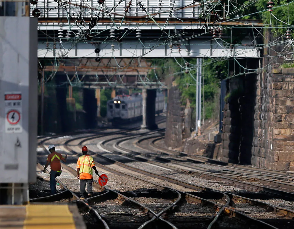 Workers walk along the tracks as a New Jersey Transit train pulls into the Trenton train station in Trenton, N.J., on July 8, 2014. (AP Photo/Mel Evans)
