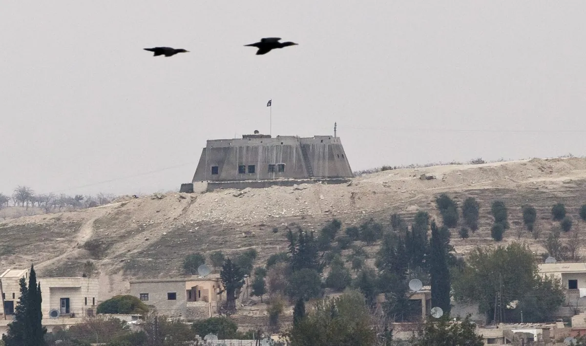 Birds fly backdropped by an building with the Islamic State group flag on top, in the Syrian city of Jarablous, seen from an archaeologic site outside Karkemish, Turkey, Saturday, Nov. 15, 2014. Archaeology and war don't usually mix, yet that's been the case for years at Karkemish, an ancient city along the Turkey-Syria border where an excavation team announced its newest finds Saturday just meters from Islamic State group-controlled territory. (AP Photo/Vadim Ghirda)