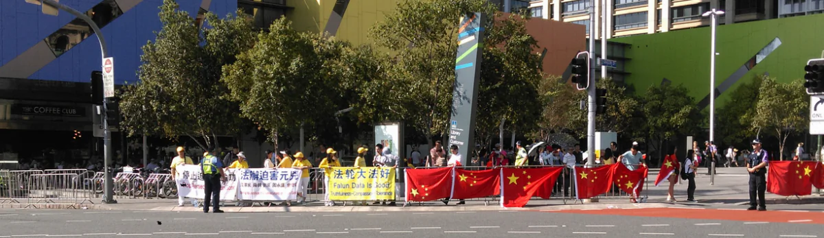 Chinese students leave their flags [one upside down] on the fence while they sit in the shade some distance away, on Saturday Nov. 15, 2014. After a large number of students tried to cover the Falun Gong banners and practitioners with the red flags the police instructed the Chinese students and their flags to move to the opposite side of the road. (Courtesy of Bethany Liu)