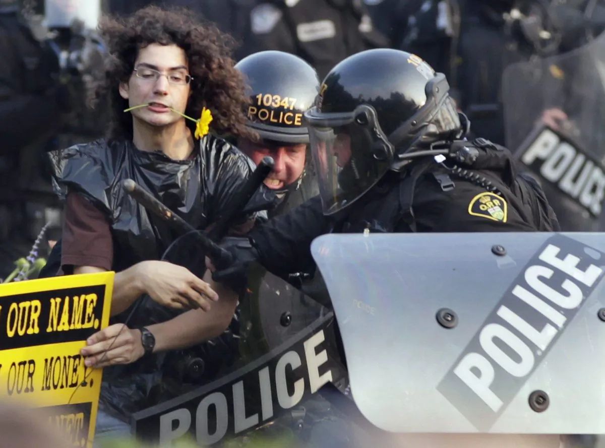 A protester with a flower clenched in his teeth is seized by riot police during protests at the G8 and G20 Summits in Toronto on June 27, 2010. A disciplinary hearing has begun for Supt. Mark Fenton, the most senior police officer charged in relation to the mass arrests during the summit. (AP Photo/Carolyn Kaster, File)