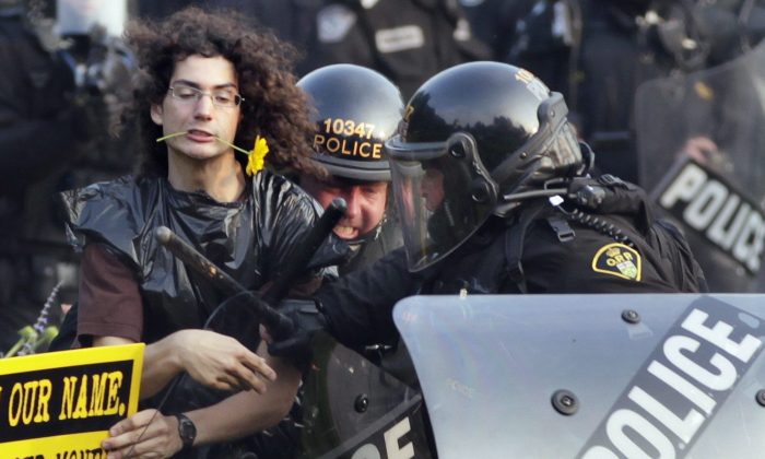 A protester with a flower clenched in his teeth is seized by riot police during protests at the G8 and G20 Summits in Toronto on June 27, 2010. A disciplinary hearing has begun for Supt. Mark Fenton, the most senior police officer charged in relation to the mass arrests during the summit. (AP Photo/Carolyn Kaster, File)