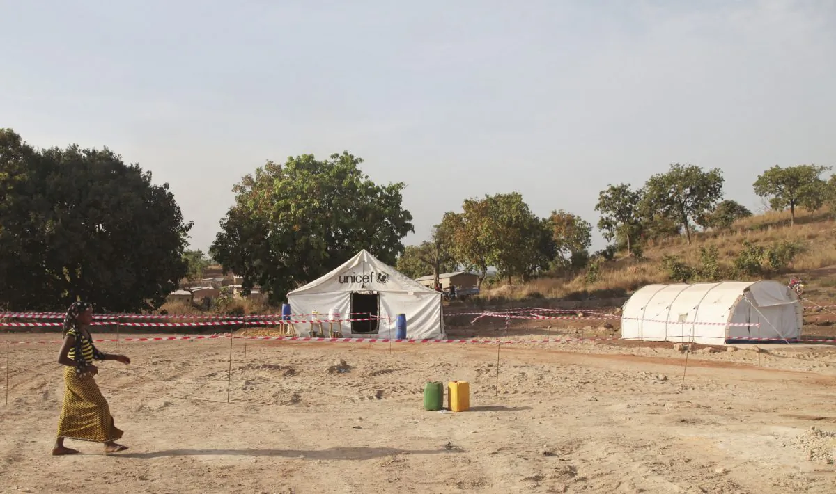 A woman walks past an Ebola healthcare center, rear, to be used for screening for Ebola virus patients at the border village of Kouremale, Mali, between Mali and Guinea, on Nov. 17, 2014. On Mali's dusty border with Ebola-stricken Guinea, travelers have a new stop: Inside a white tent, masked medical workers zap incomers with infrared thermometer guns and instruct them to wash their hands in chlorinated water. (AP Photo/Baba Ahmed)