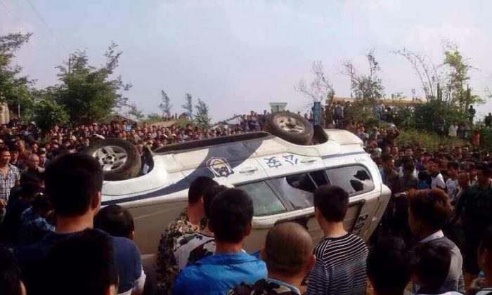 Protesters stand around an upside down police vehicle in Haikou, Hainan Province, China, on Nov. 18. A mass protest against construction of a prevention center in Haikou, Hainan Province turned into a clash with police shooting rubber bullets and protesters smashing the police vehicles, on Nov. 18, 2014. (Internet photo)
