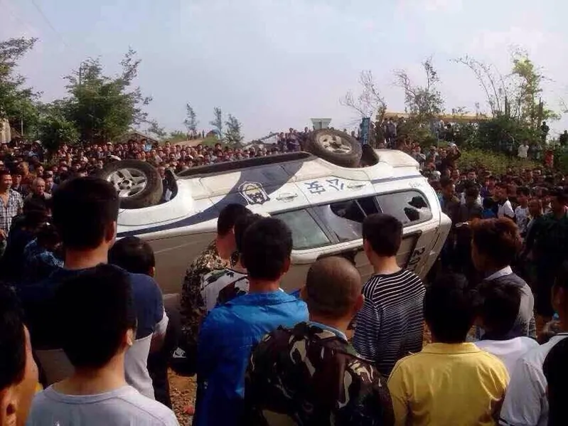 Protesters stand around an upside down police vehicle in Haikou, Hainan Province, China, on Nov. 18. A mass protest against construction of a prevention center in Haikou, Hainan Province turned into a clash with police shooting rubber bullets and protesters smashing the police vehicles, on Nov. 18, 2014. (Internet photo)