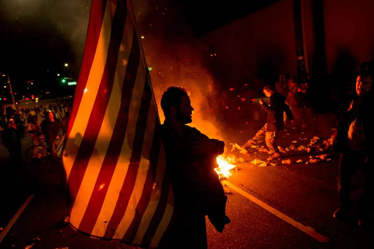 James Cartmill holds an American flag while protesting in Oakland, Calif., on Monday, Nov. 24, 2014, after the announcement that a grand jury decided not to indict Ferguson police officer Darren Wilson in the fatal shooting of Michael Brown, an unarmed 18-year-old. Several thousand protesters marched through Oakland with some shutting down freeways, looting, burning garbage and smashing windows. (AP Photo/Noah Berger)