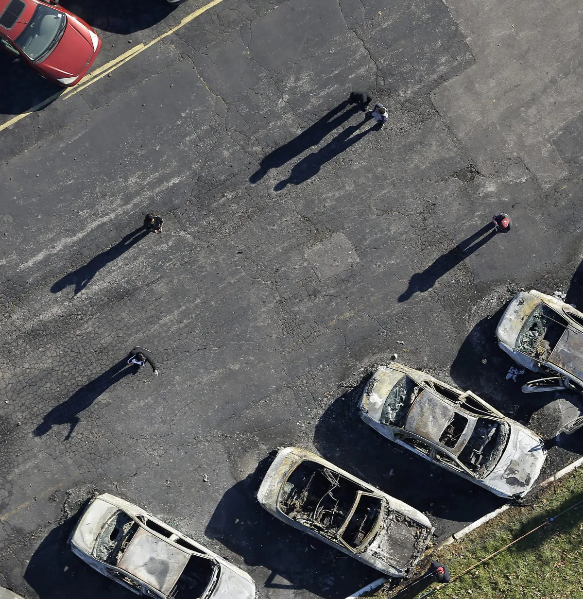 In this aerial photo, people look at a row of charred cars at a used car dealership, Tuesday, Nov. 25, 2014, in Dellwood, Mo., after they were burned in overnight protests following a grand jury's decision not to indict a white police officer in the killing of unarmed black 18-year-old Michael Brown. Monday night's protests were far more destructive than any of those that followed Brown's Aug. 9 death, with more than a dozen businesses badly damaged or destroyed. (AP Photo/Charlie Riedel)