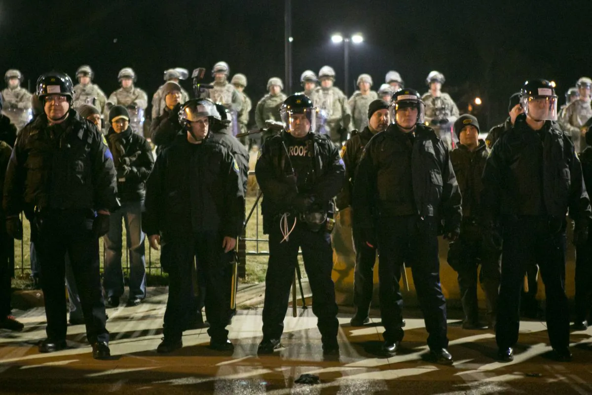 The police and the National Guard stand alert as activists across the street stage a protest in front of the Ferguson Police Station, Mo., on Nov. 25, 2014. (Benjamin Chasteen/Epoch Times)