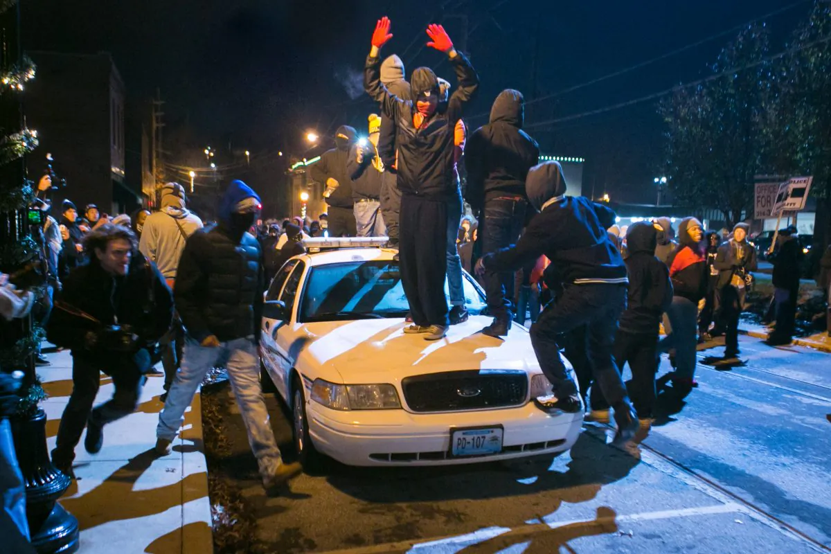 Activists stand and jump on a police car before hurling rocks and lighting it on fire in Ferguson, Mo., on Nov. 25, 2014. (Benjamin Chasteen/Epoch Times)