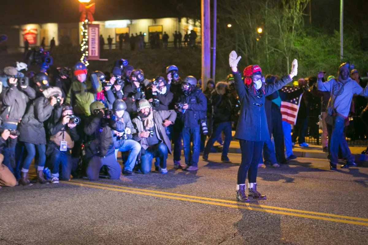 A lone woman stands with her hands up in front of the police making an announcement for her to leave the street, as media take shots of her from behind, in Ferguson, Mo., on Nov. 25, 2014. (Benjamin Chasteen/Epoch Times)