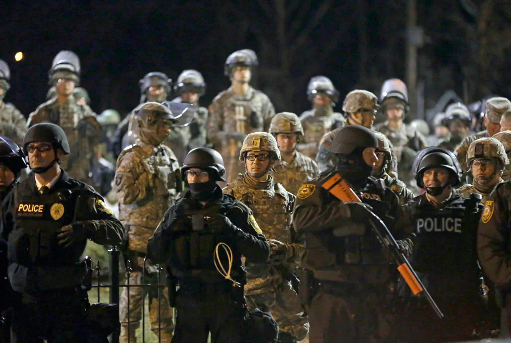 Police and Missouri National Guardsmen stand guard as protesters gather in front of Ferguson Police Department on Friday, Nov. 28, 2014, in Ferguson, Mo. Several protesters have been taken into custody during a demonstration outside the police department. Tensions escalated late Friday during an initially calm demonstration after police said protesters were illegally blocking West Florissant Avenue. (AP Photo/Jeff Roberson)