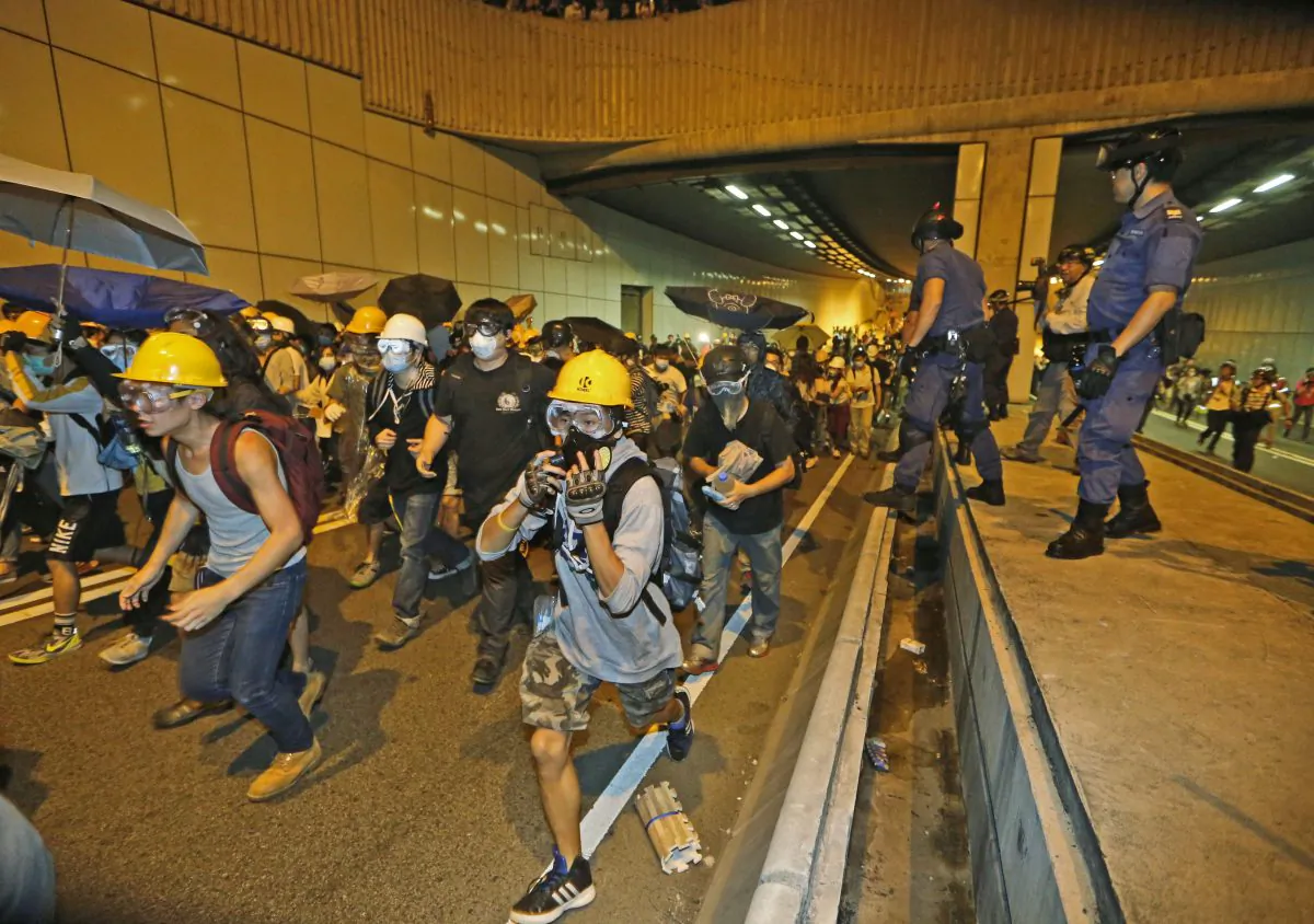 Pro-democracy protesters run away from police on the main road outside the government headquarters in Hong Kong Sunday, Nov.30, 2014. Hundreds of pro-democracy protesters faced off with Hong Kong police late Sunday, stepping up their movement for genuine democratic reforms after being camped out on the city's streets for more than two months. (AP Photo/Kin Cheung)