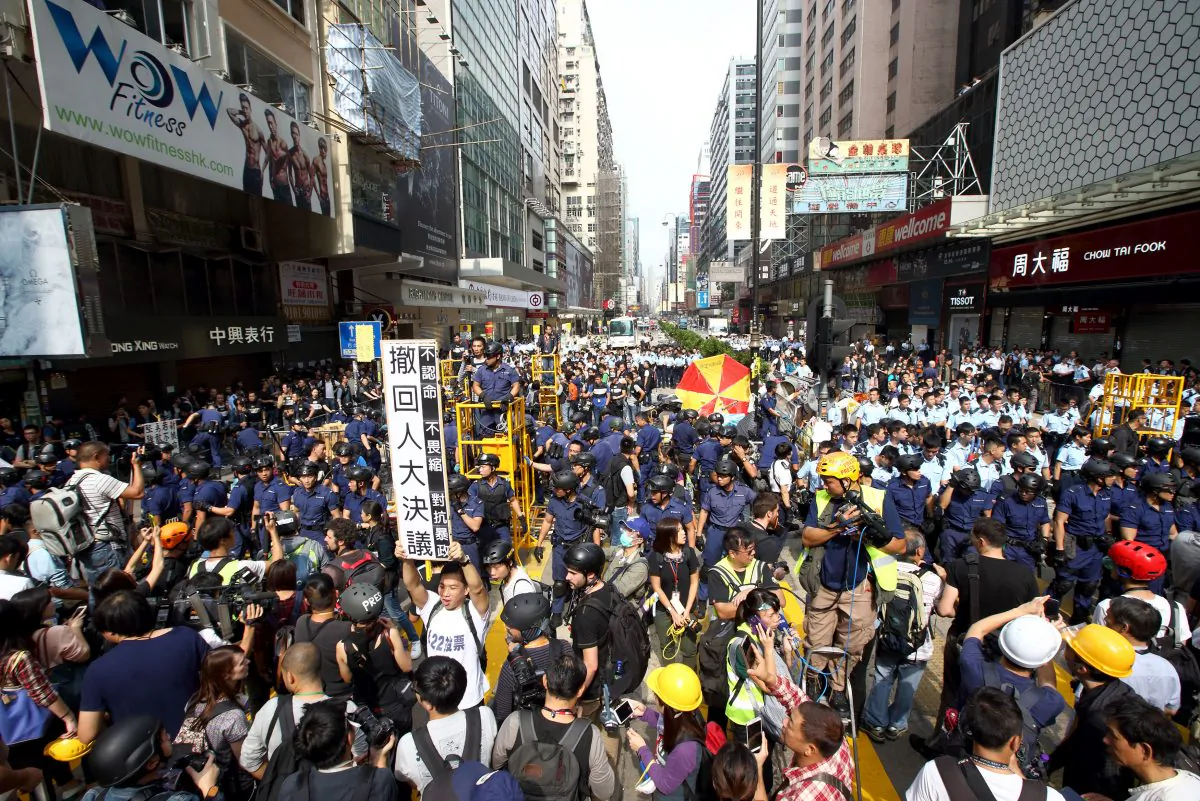 During police clearance of the Mong Kok protest site, a protester in white tee-shirt is holding a placard demanding the authority to take back NPC’s decision on HK universal suffrage, Nov. 26, 2014. (C.S. Poon/Epoch Times)