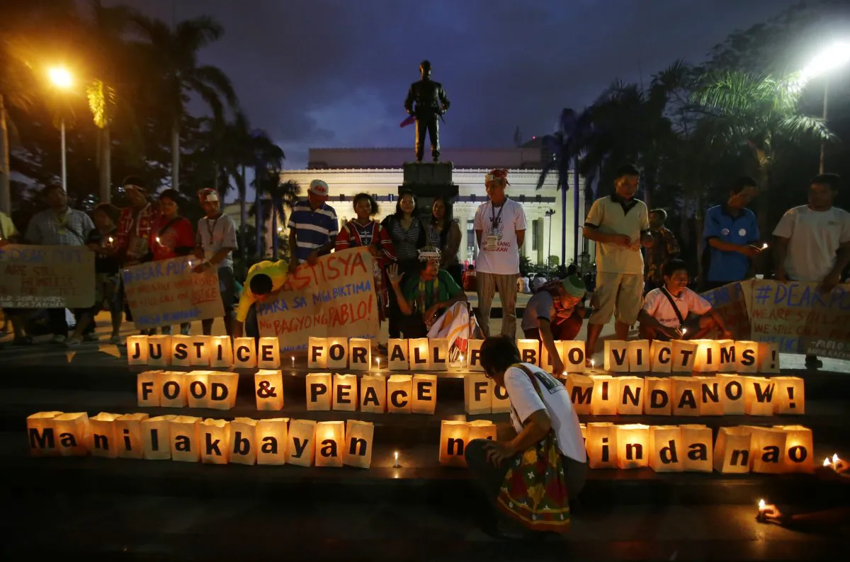 Filipino activists and typhoon survivors stand beside candles inside paper boxes as they mark the second year anniversary when Typhoon Bopha struck the country during a rally in Manila, Philippines on Thursday, Dec. 4, 2014. Typhoon Bopha, locally named Pablo, left hundreds of people dead and rendered extensive damage to agriculture in southern Philippines in 2012. (AP Photo/Aaron Favila)