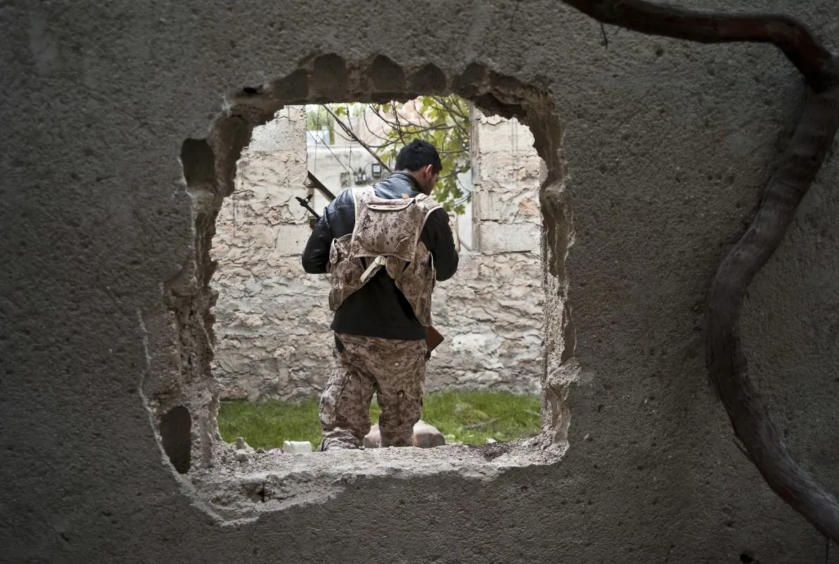 In this Nov. 1, 2014 photo, a fighter from the coalition against the Islamic State group is seen through a hole cut in a wall to create shortcuts in the battlefield in Kobani, Syria. In a surprising display of resilience, the Kurdish fighters have held out against the more experienced jihadists more than two months into the Islamic State group militants' offensive on the frontier town, hanging on to their territory against all expectations.(AP Photo/Jake Simkin)