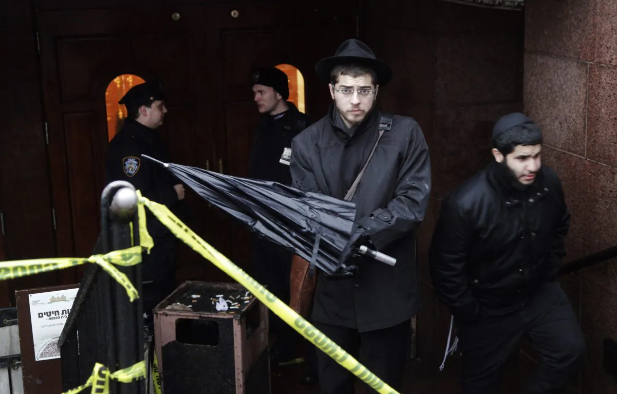 A member of the Lubavitch community, center, leaves the Chabad-Lubavitch Hasidic headquarters guarded by members of the New York Police Department, left, Tuesday, Dec. 9, 2014, in New York.  (AP Photo/Mark Lennihan)
