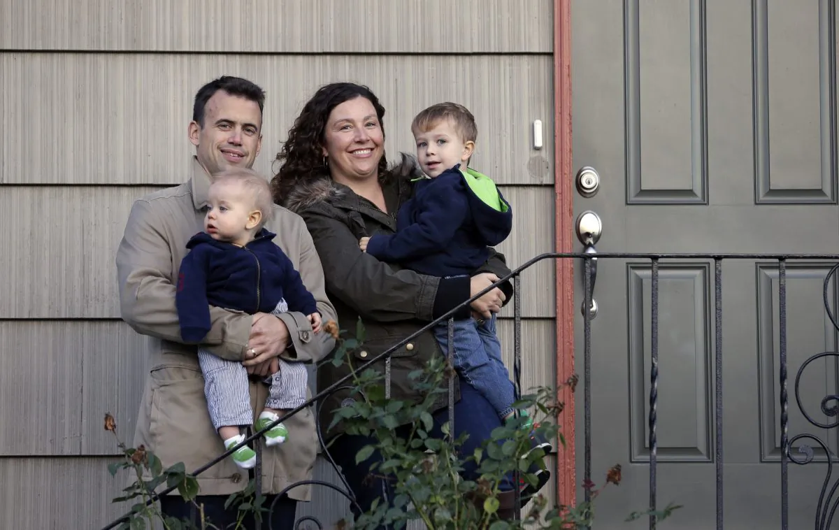 Jennifer Ewing, and her husband Florian Thiel hold their children Max (R), 3, and Felix, 8-months, as they pose for a photo on the steps of their new home in Seattles Ballard neighborhood, on Oct. 15, 2014. The couple recently closed on the three-bedroom house , which cost slightly less than $500,000. They moved to Seattle from New York, another city that matches the pattern of high-income jobs and even more expensive housing. (AP Photo/Elaine Thompson)