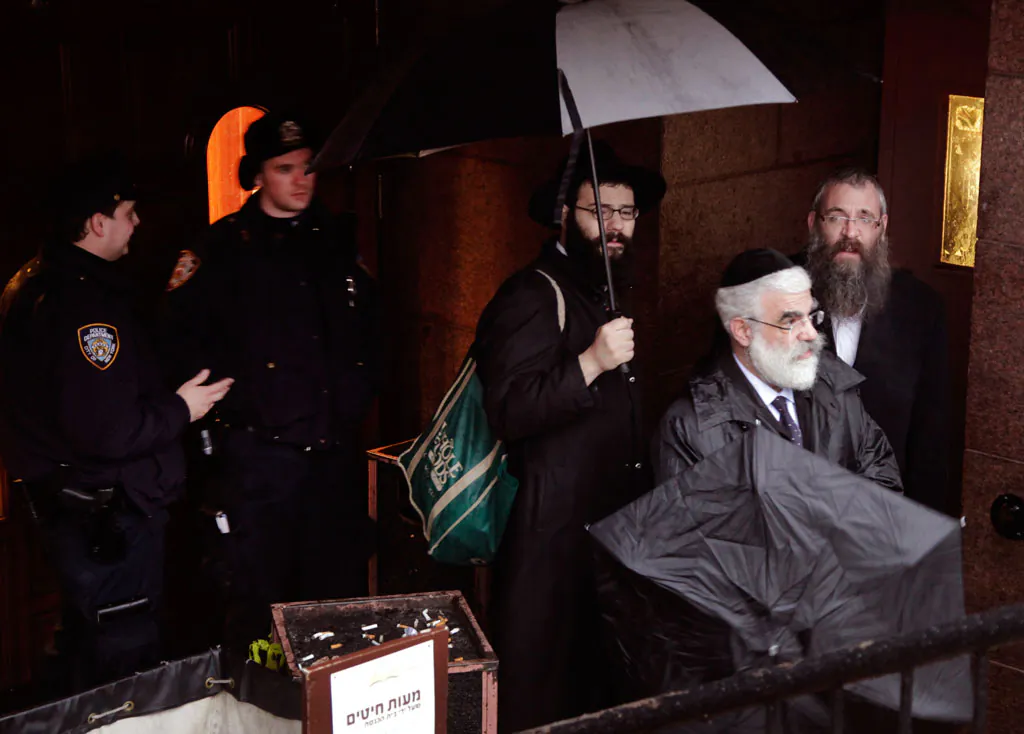 Members of the Lubavitch community leave Chabad-Lubavitch Hasidic headquarters being guarded by police officers (L) in New York on Tuesday, Dec. 9, 2014. Earlier a knife-wielding man stabbed an Israeli student inside the Brooklyn synagogue before being fatally shot by police after he refused to drop the knife. (AP Photo/Mark Lennihan)