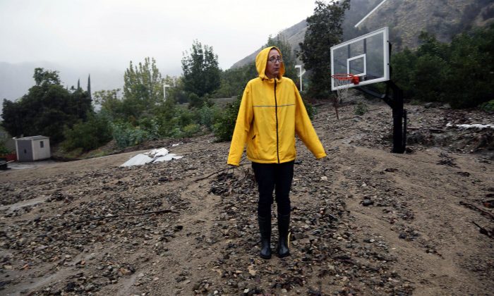 Homeowner Amanda Heinlein stands on a mud landslide covering a basketball court near her house in Azusa, Calif., Friday, Dec. 12, 2014.   A soaking storm swept into  California, causing several mudslides, flooding streets and cutting power to tens of thousands Friday after lashing the rest of the state with much-needed rain.   (AP Photo/Nick Ut)