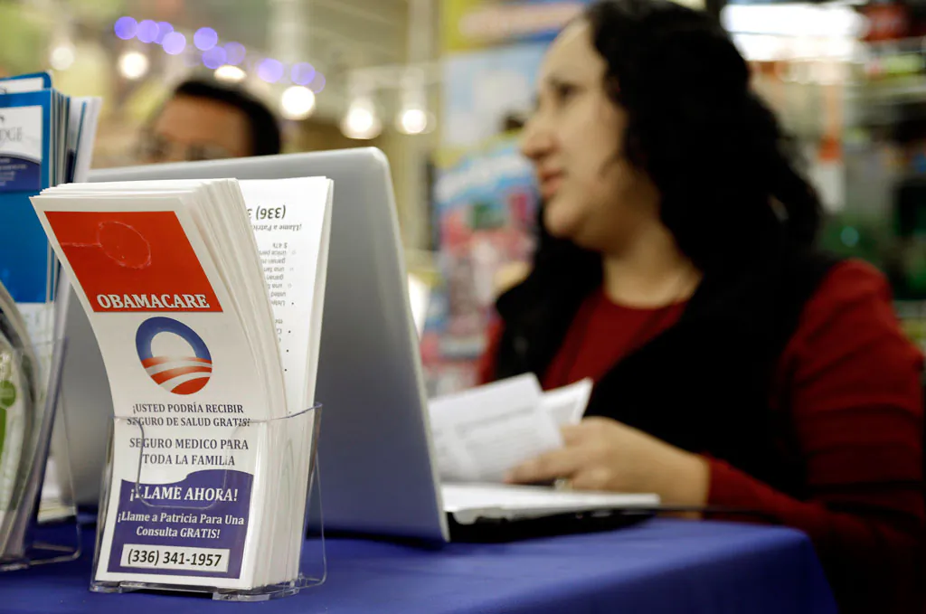 In this photo taken Saturday, Nov. 22, 2014, Blue Bridge Benefits LLC agent Patricia Sarabia helps customers interested in Obama Care at a kiosk at Compare Foods in Winston-Salem, N.C. Such atypical approaches to selling health insurance policies are playing out across the country since the second round of open enrollment under the federal Affordable Care Act opened in mid-November. Insurance companies and some states are focusing heavily on signing up eligible Hispanics, a group that accounts for a large share of the nation's uninsured but largely avoided applying for coverage during the first full year the health care reform law was in effect. Hispanics accounted for just 11 percent of those who enrolled in the private policies sold during the initial sign-up period, which ended in March. (AP Photo/Gerry Broome)