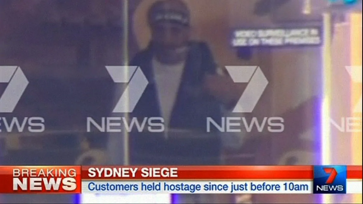 This image taken from video shows a man believed to be a gunman inside a cafe in Sydney, Australia Monday, Dec. 15, 2014. An apparent hostage situation was unfolding inside the chocolate shop and cafe in Australia's largest city on Monday, where several people could be seen through a window with their hands held in the air. (AP Photo/Channel 7 via AP Video) 