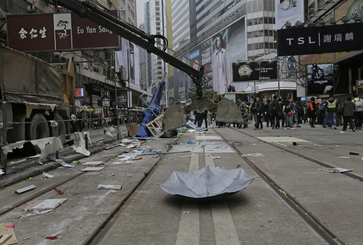An excavation shovel is lowered to pick up an umbrella left behind by protesters as police clear barricades and tents on a main road in the occupied areas at Causeway Bay district in Hong Kong Monday, Dec 15, 2014. (AP Photo/Vincent Yu)