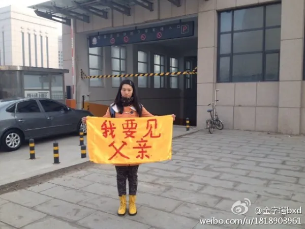 College girl Bian Xiaohui holds a banner that says "I want to see my father" on street on March 3, 2014. Bian and her cousin who took the photo have been detained, and went on trial on Dec. 12 being accused for "publicizing Falun Gong persecution" by putting the photo online. (Screenshot/Weibo.com)