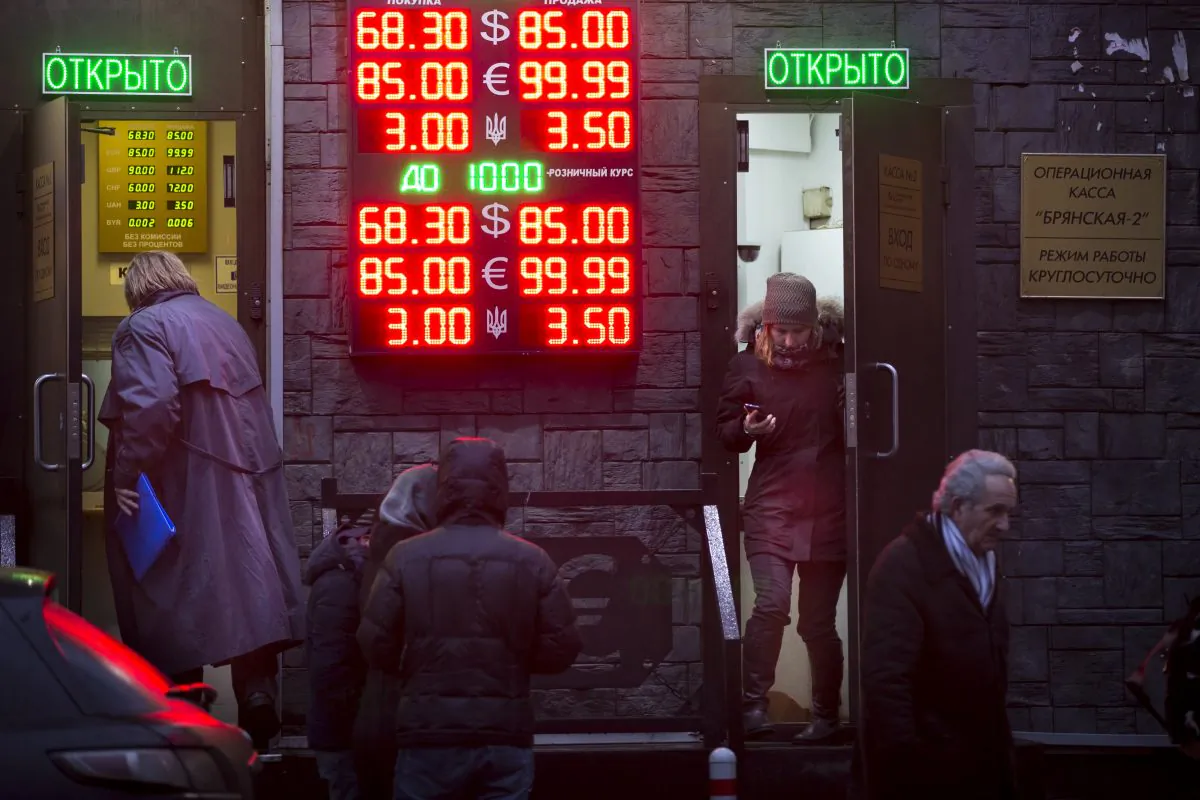 People wait to exchange their currency as signs advertise the exchange rates at a currency exchange office in Moscow, Russia, Tuesday, Dec. 16, 2014. The Russian ruble came under intense selling pressure Tuesday, falling at one point by a catastrophic 20 percent to a new historic low despite a massive pre-dawn interest rate hike from Russia's Central Bank. Russian officials were clearly rattled even though state television urged citizens not to panic.The top two figures indicate the spread on the dollar-ruble rate and the middle two figures indicate the euro-ruble rate, with the third showing the spread on the Ukrainian hryvnia-ruble rate. (AP Photo/Alexander Zemlianichenko)