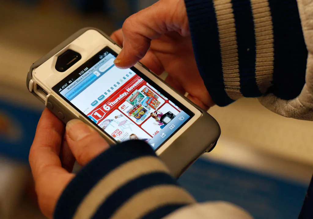 A Target shopper uses her iPhone to compare prices at Wal-Mart while shopping after midnight in South Portland, Maine, on Nov. 28, 2014. (AP Photo/Robert F. Bukaty)