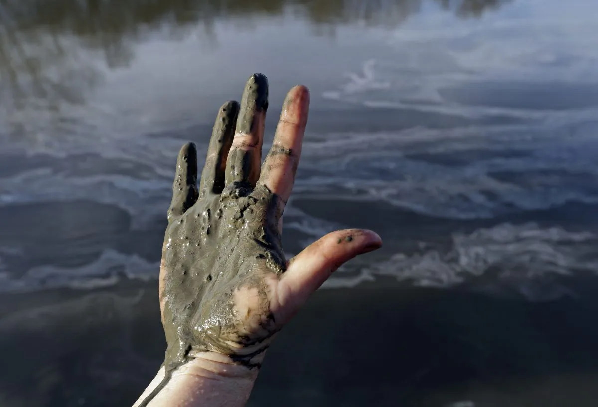 Amy Adams, North Carolina campaign coordinator with Appalachian Voices, shows her hand covered with wet coal ash from the Dan River swirling in the background, in Danville, Va., Feb. 5, 2014. (AP Photo/Gerry Broome)
