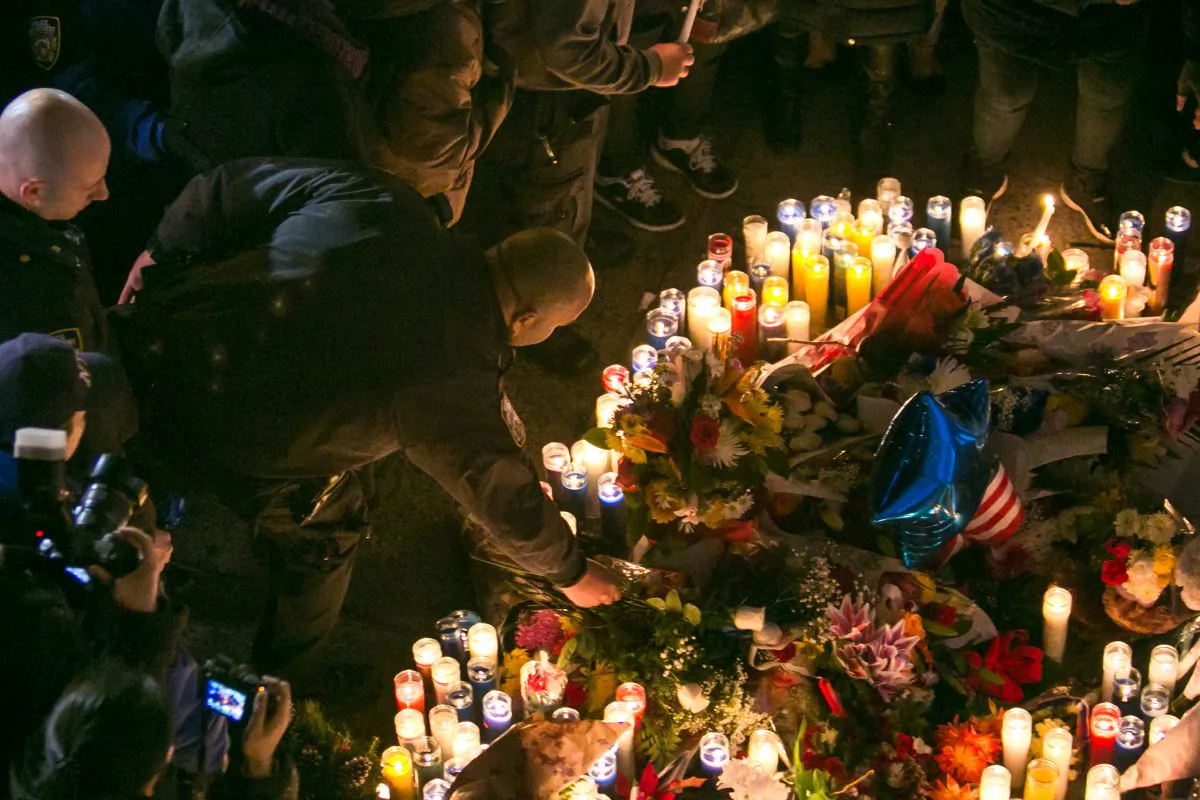 A NYPD police officer lays a flower at a memorial on Dec. 21, 2014 for the two police officers who were shot and killed in their car in Brooklyn, New York, the day before. (Benjamin Chasteen/Epoch Times)