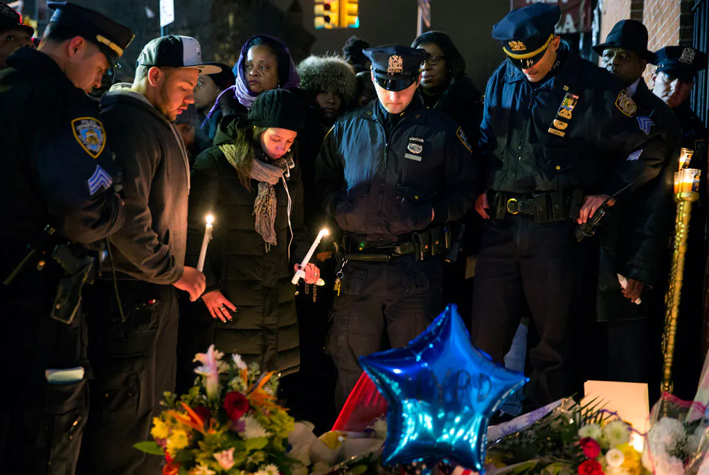 Police officers and other mourners stand in silence, Sunday, Dec. 21, during a candlelight vigil near the spot where two New York Police Department officers, sitting inside a patrol car the previous day, were shot by an armed man, killing them both. The assailant then went into a nearby subway station and committed suicide, police said. (AP Photo/Craig Ruttle)