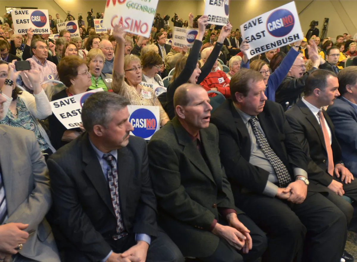 Officials from the Howe Caverns group react as people opposed to a casino hold up signs in East Greenbush, N.Y., on Dec. 17, 2014. Work on new casinos planned for upstate New York won’t begin until environmental reviews and casino executive background checks are completed. (AP Photo/The Troy Record, Mike McMahon)