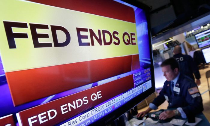 A specialist works at his post on the floor of the New York Stock Exchange, as a television screen shows the decision of the Federal Reserve to end quantitative easing, on Oct. 29, 2014. (AP Photo/Richard Drew)