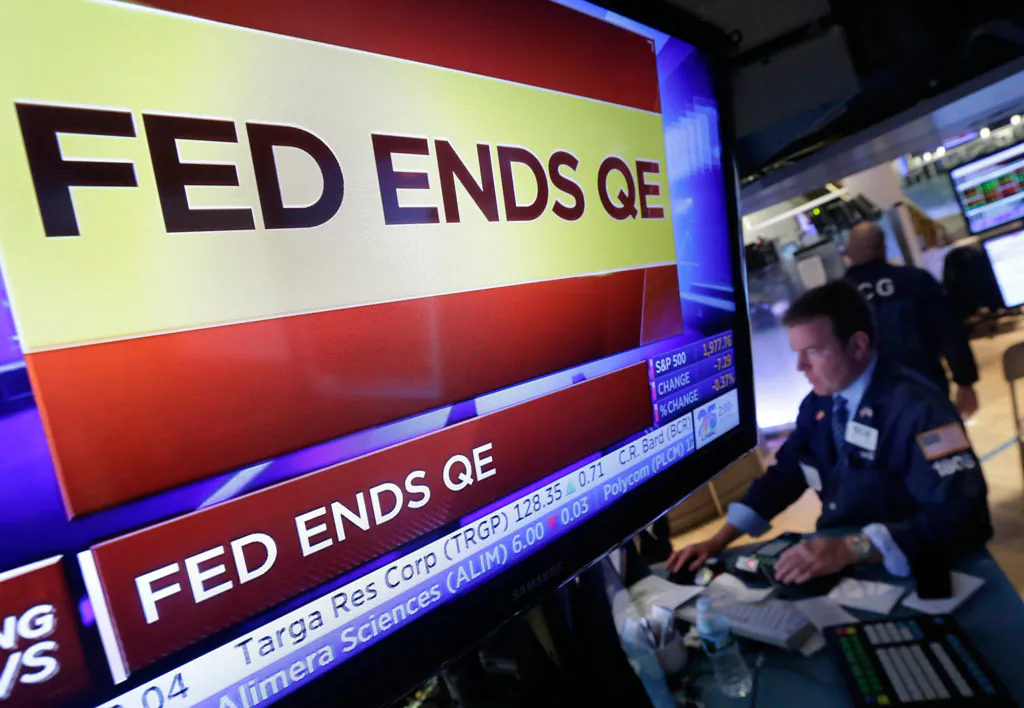 A specialist works at his post on the floor of the New York Stock Exchange, as a television screen shows the decision of the Federal Reserve to end quantitative easing, on Oct. 29, 2014. (AP Photo/Richard Drew)