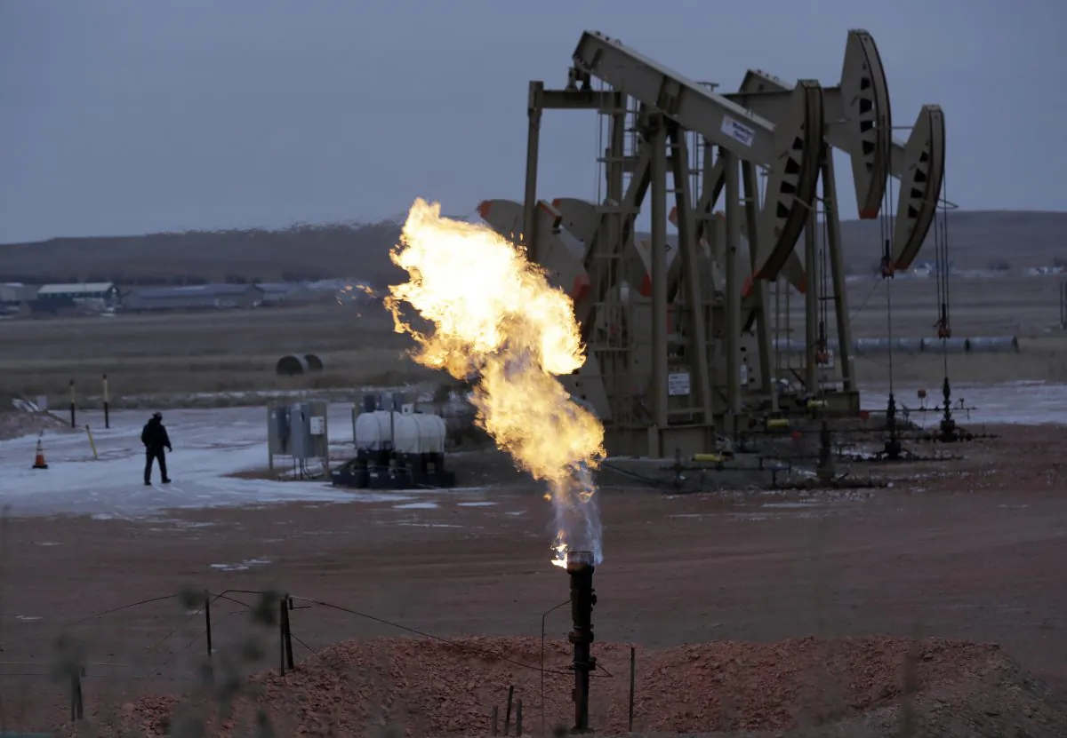 Workers tend to oil pump jacks behind a natural gas flare near Watford City, N.D., on Dec. 17, 2014. Natural gas, the nation's most prevalent heating fuel, is getting cheaper just as winter is arriving because of mild temperatures and plentiful supplies. (AP Photo/Eric Gay)