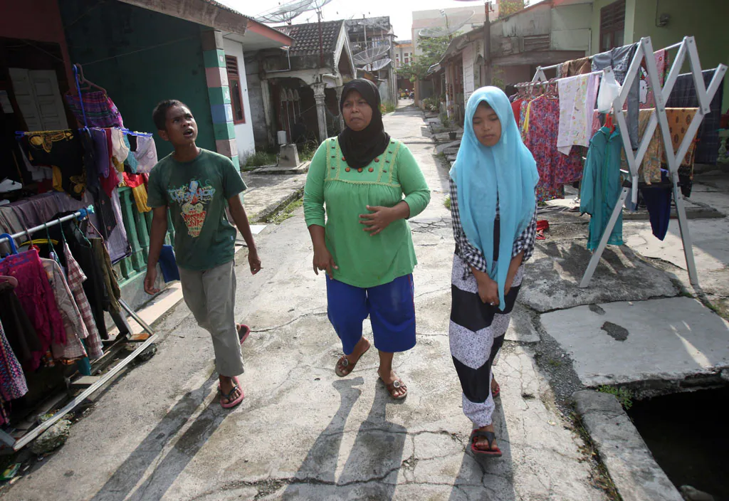 Tsunami survivor Jamaliah (C) walks with Raudhatul Jannah (R) and Arif Pratama, whom she believes to be her two children separated with her when the village they lived in was hit by the killer waves in 2004, in their neighborhood in Meulaboh, Aceh province, Indonesia, on Oct. 21, 2014. Although there has been no DNA test the parents are convinced that the children belong them. (AP Photo/Binsar Bakkara)