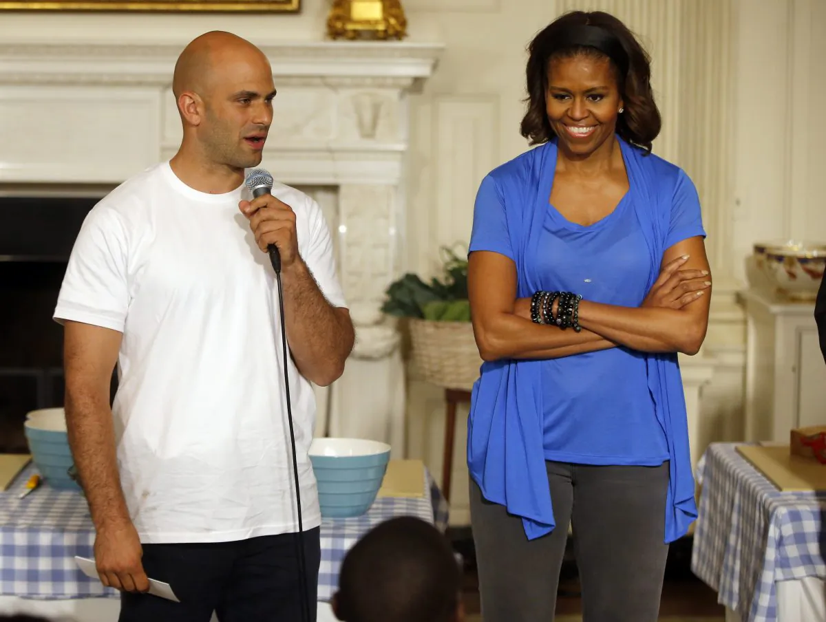 First lady Michelle Obama stands with Sam Kass, White House Senior Policy Adviser for Nutrition Policy, before they make salads from vegetables harvested from the White House garden with area students in the State Dining Room of the White House in Washington on June 12, 2104. President Barack Obama’s personal chef is leaving after nearly six years in which, unlike any assistant White House chef before him, he cooked up policy alongside his meals. Kass held the title of senior policy adviser for nutrition policy, which gave him a seat at the table to help administration officials hash out everything from an updated “Nutrition Facts” label for processed foods to new government standards to cut the amount of fat, calories and sodium in federally subsidized school meals. (AP Photo/Charles Dharapak)