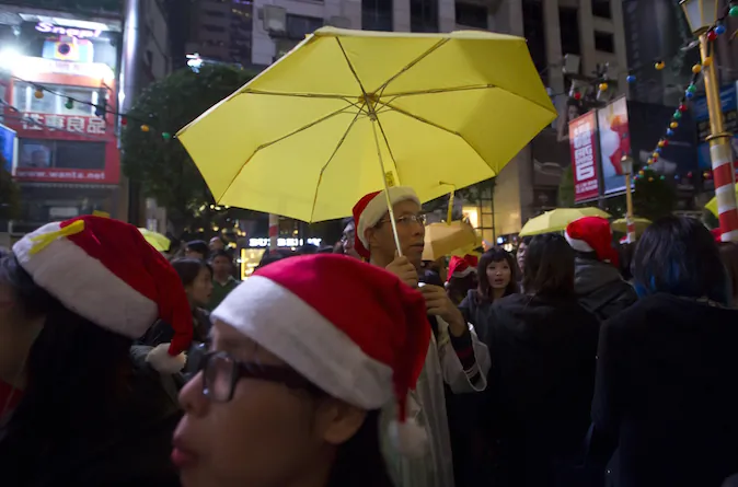 The guy in the Christmas hat and holding the yellow umbrella is clearly both merrymaker and protester... or neither?!? (AP Photo/Kin Cheung)
