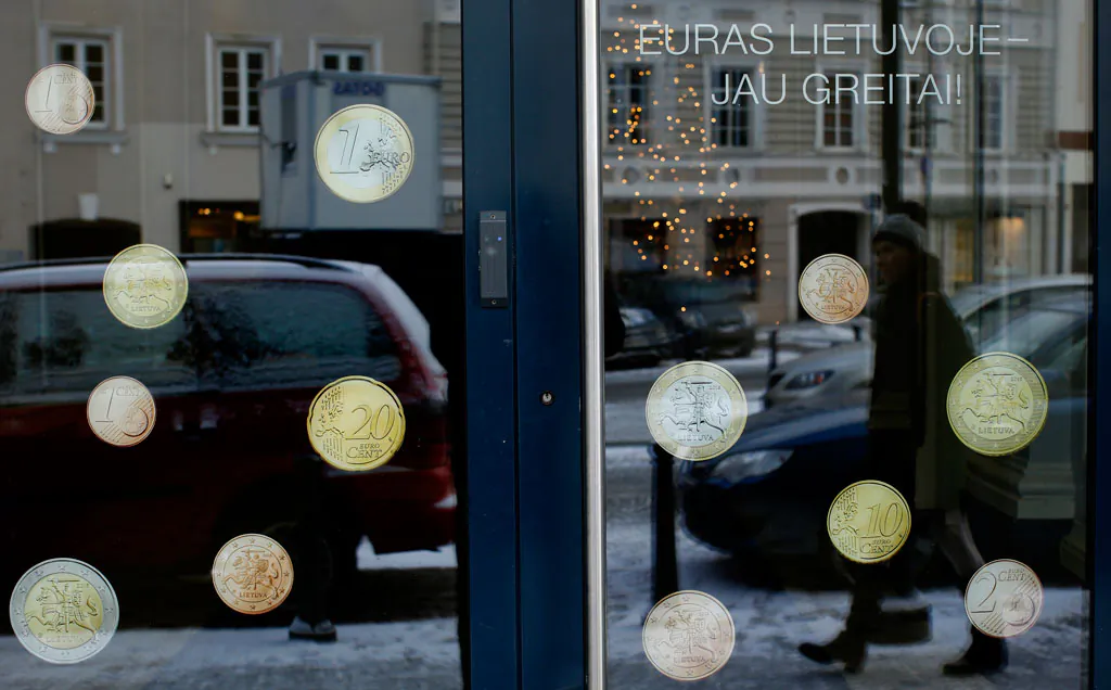 A pedestrian is reflected in a window decorated with Lithuanian promo Euro coins with inscription "The euro is coming soon to Lithuania " in Vilnius, Lithuania, Monday, Dec. 29, 2014. Political leaders are hoping that joining the euro on Jan. 1 will help Lithuania distance itself further from Russian influence and reduce government borrowing costs. (AP Photo / Mindaugas Kulbis)