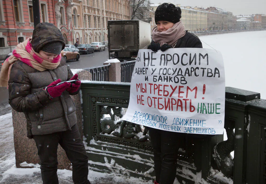 Oksana Li (R) stands with her son Gleb, 12, in a one-person picket, holding a poster reading "We are not asking for money from the state and banks, we demand not to take ours!" in St.Petersburg, Russia, on Dec. 28, 2014. Oksana went to a one-person picket to protest the onerous foreign currency mortgage that threatens to ultimately deprive thousands of the country’s mortgage borrowers of their apartments amid Russia’s economic crisis. (AP Photo/Dmitry Lovetsky)