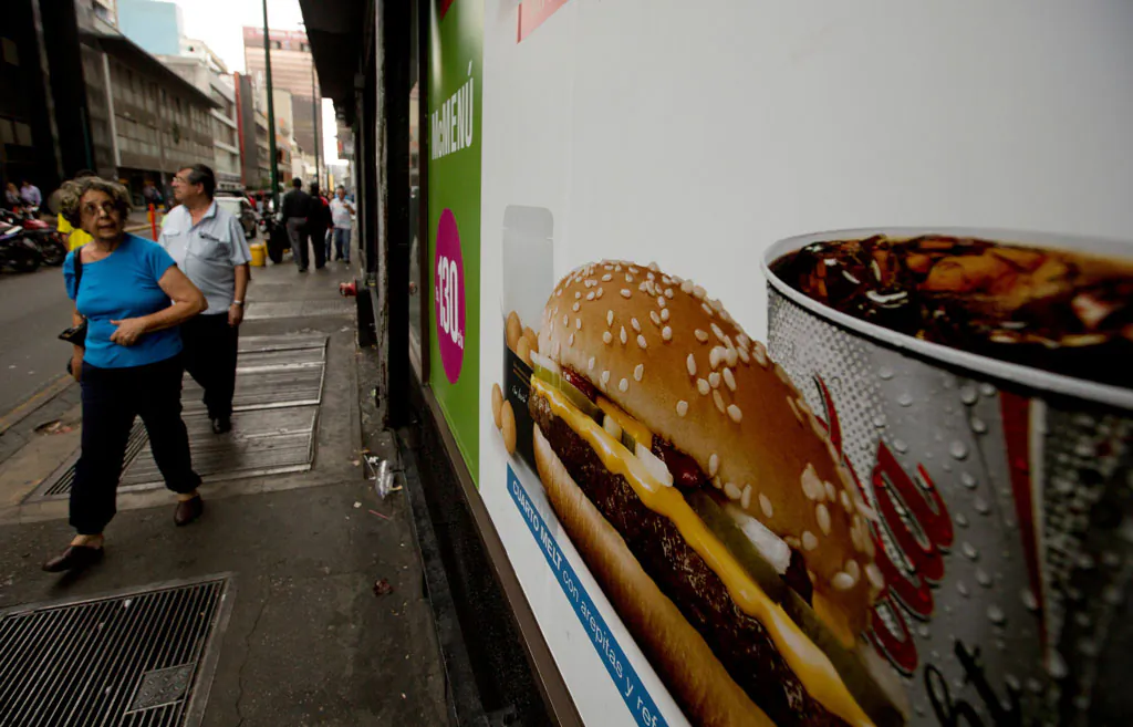 A customer glances at a McDonalds' banner menu showing a burger accompanied by arepas or corn cakes, instead of fries, in Caracas, Venezuela, Tuesday, Jan. 6, 2015. McDonald’s franchises in Venezuela have run out of potatoes and are now serving South American alternatives like deep-fried arepas or yuca, a starchy tuberous root. The franchisers are blaming a contract dispute with West Coast dock workers for halting the export of frozen fries to the country. (AP Photo/Fernando Llano)