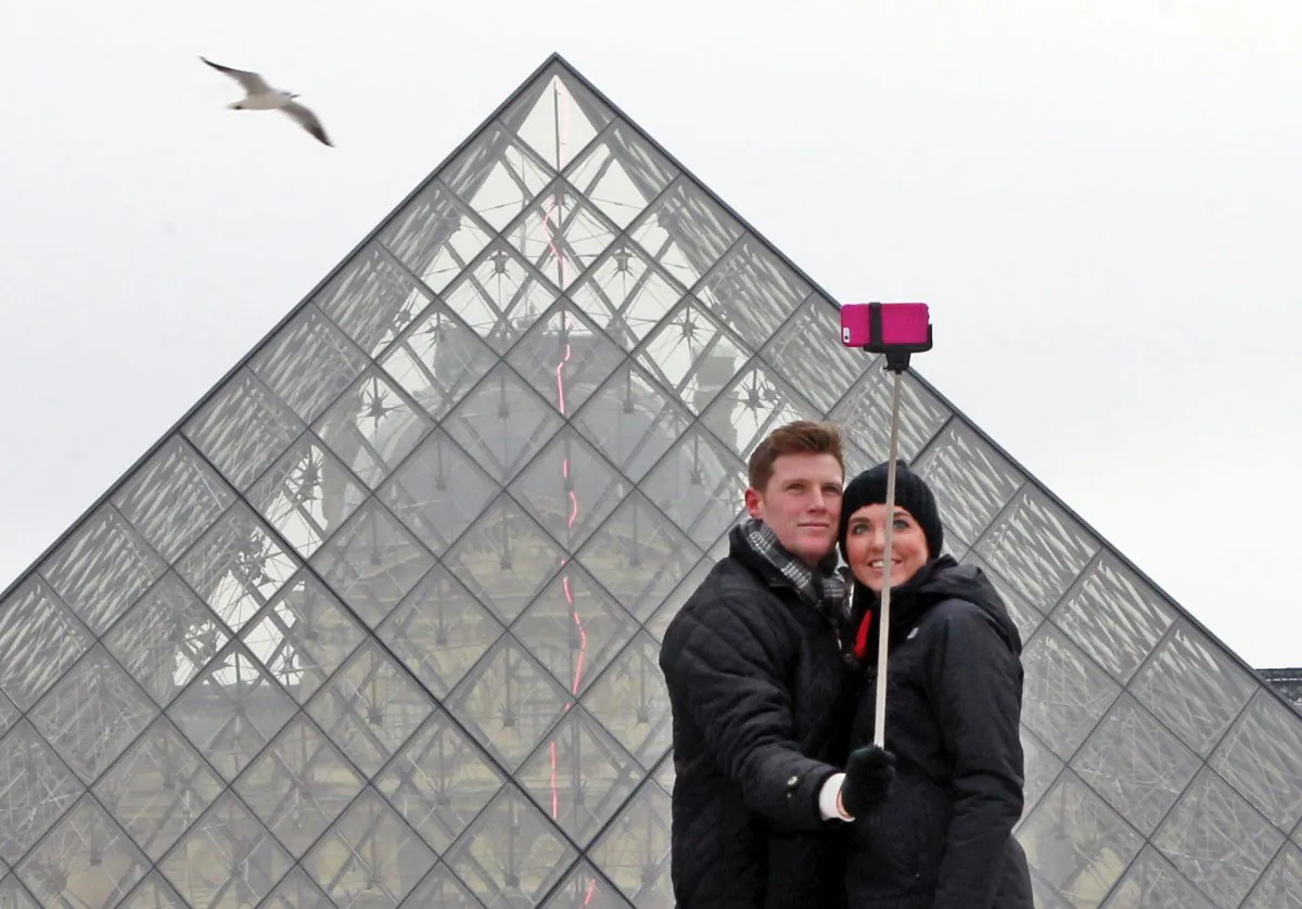 Chris Baker and Jennifer Hinson from Nashville, Tennessee, use a selfie stick in front of the Louvre Pyramide in Paris, Tuesday, Jan. 6, 2015. (AP Photo/Remy de la Mauviniere)