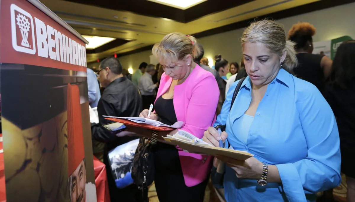 Job seekers Madelin Garcia (R) and Noharis Nunez fill out a job applications near a Benihana booth at a job fair in Miami Lakes, Fla., on Oct. 22, 2014. With the price of oil below $50 a barrel, consumers will have steadily more money to spend, potentially creating job openings at retailers, auto dealers, shipping firms, restaurants and hotels. (AP Photo/Alan Diaz)
