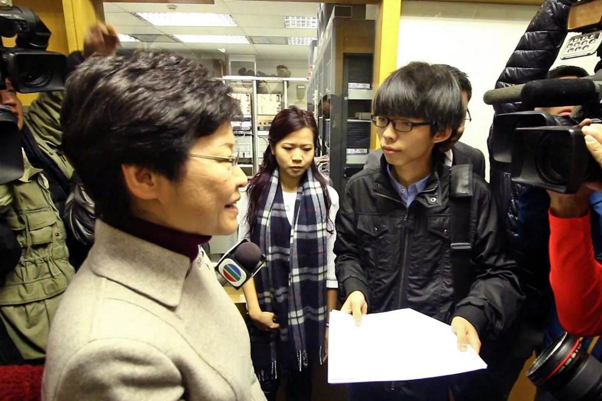 Scholarism leader Joshua Wong hands Chief Secretary Carrie Lam a junior high grading guide at the Commercial Radio office on Thurs., Jan. 8, 2015. (Choi Man Man/Epoch Times)