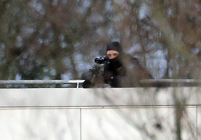 A hooded police officer aim from a rooftop in Dammartin-en-Goele, northeast of Paris, where the two brothers suspected in a deadly terror attack were cornered, Friday, Jan. 9, 2015. Two sets of attackers seized hostages and locked down hundreds of French security forces around the capital on Friday, sending the city into fear and turmoil for a third day in a series of linked attacks that began with the deadly newspaper terror attack that left 12 people dead. (AP Photo/Christophe Ena)